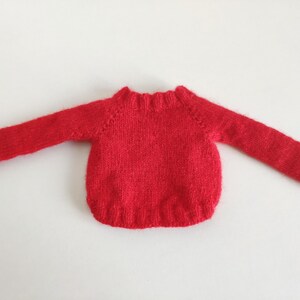 May include: Red knitted sweater with long sleeves and a crew neck.
