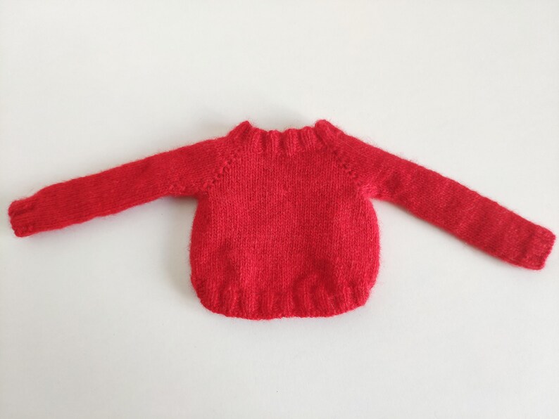May include: Red knitted sweater with long sleeves and a crew neck.