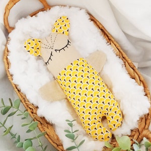 May include: A yellow and brown fabric stuffed animal with a simple face and closed eyes. The animal is lying in a wicker basket lined with white fur.