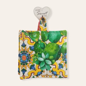 May include: A white, yellow, blue and green pot holder with a cactus and floral pattern. The pot holder has a loop for hanging and a heart-shaped tag that says "Home Sweet Home".