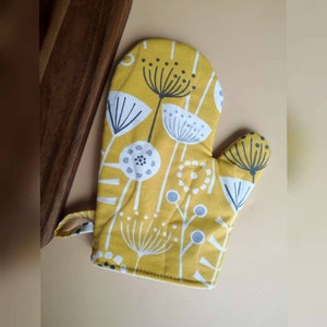 May include: Yellow oven mitt with a white and gray floral pattern. The mitt has a loop for hanging.