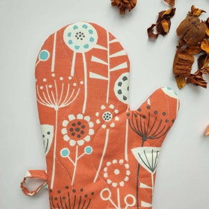 May include: Orange oven glove with a floral pattern in white, black and blue. The glove has a hanging loop.