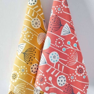 May include: Two kitchen towels with a floral pattern. One towel is yellow with a white and gray floral design. The other towel is red with a white and blue floral design.