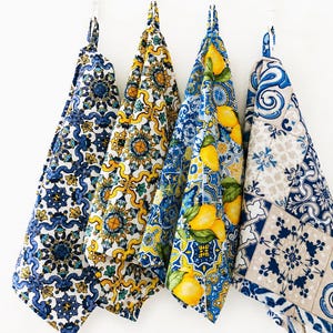 May include: Four hanging kitchen towels featuring distinct patterns. The first has blue and white geometric motifs. The second displays yellow and blue floral designs. The third shows yellow lemons with blue foliage. The fourth features blue and beige tiles.