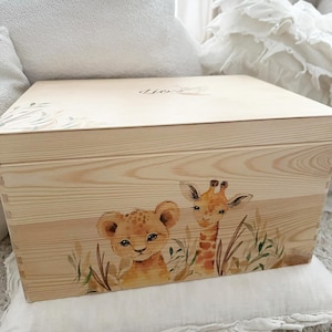 Könnte beinhalten: Eine Holzkiste mit handgemaltem Design eines Löwen und einer Giraffe in einer Dschungelkulisse. Die Kiste ist hellbraun und hat einen Deckel mit dem Wort "Lion" darauf.