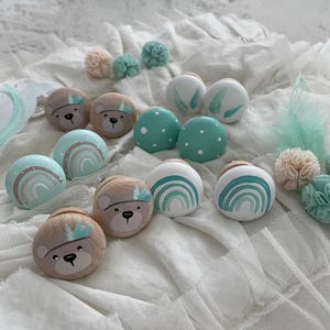 Könnte beinhalten: Ein Set mit 10 Holzgriffen mit verschiedenen Designs, darunter Bären, Regenbögen und Federn. Die Griffe sind in Blautönen und Grüntönen mit weißen Akzenten bemalt.