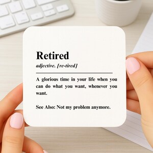 May include: A square, white coaster with the definition of "Retired" printed in black. The definition includes the phrase "Not my problem anymore."