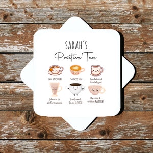 Op de afbeelding: Witte keramische onderzetter met de tekst "SARAH'S Positive Tea" en zes geillustreerde theekopjes met positieve affirmaties. De affirmaties zijn: "I am ENOUGH!", "I've GOT this", "I am talented & intelligent", "I deserve to ask for my needs", "I am Loved! So. so LOVED!" en "My voice & opinion MATTER!"