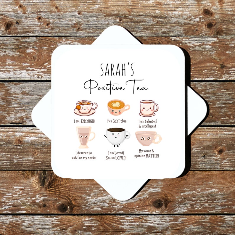 Op de afbeelding: Witte keramische onderzetter met de tekst "SARAH'S Positive Tea" en zes geillustreerde theekopjes met positieve affirmaties. De affirmaties zijn: "I am ENOUGH!", "I've GOT this", "I am talented & intelligent", "I deserve to ask for my needs", "I am Loved! So. so LOVED!" en "My voice & opinion MATTER!"