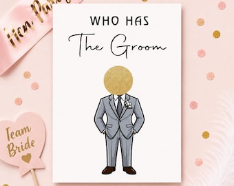 May include: A white rectangular game card with the text WHO HAS The Groom in black font. Below the text is an illustration of a figure in a grey suit with a gold glitter circle covering the head, positioned above a heart-shaped sign with Team Bride.
