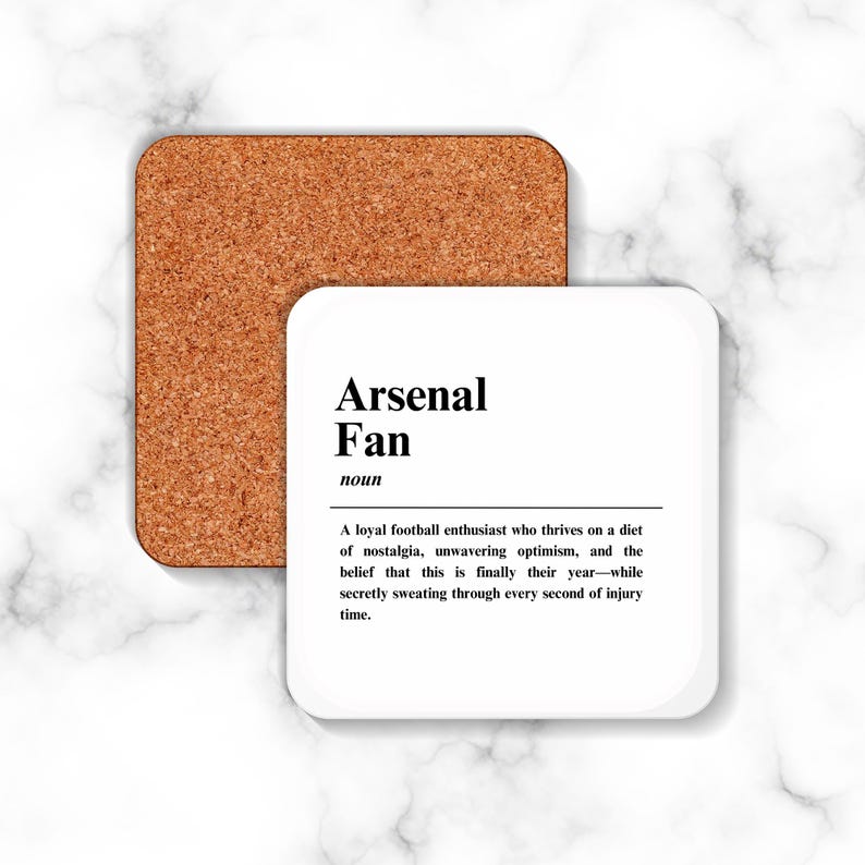 May include: White coaster with black text defining an Arsenal Fan as a loyal football enthusiast who thrives on nostalgia, unwavering optimism, and the belief that this is finally their year, while secretly sweating through every second of injury time.