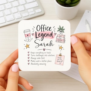 May include: A square white coaster featuring the text Office Legend Sarah in black script, surrounded by illustrations of a coffee cup, a potted plant on books, stars, and a checklist of positive traits, plus a pink note saying Thank you for being you.