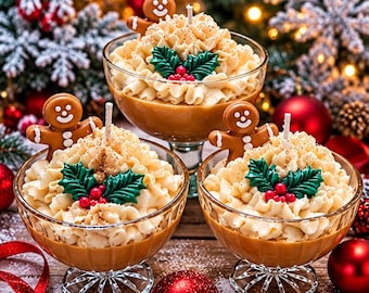 May include: Three glass dessert cups filled with tan wax, topped with piped cream-colored wax swirls, a brown gingerbread man figure, and green holly leaves with red berries. Each candle features a central white wick and a dusting of brown spice.