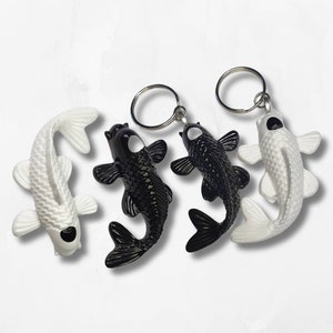 May include: Three keychains featuring black and white koi fish. The koi fish are attached to silver key rings.