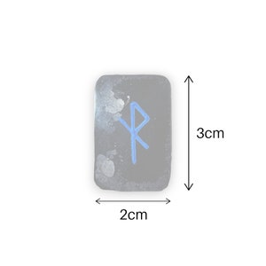May include: A small, black, rectangular stone with a blue rune symbol painted on it. The stone measures 2 inches by 3 inches.