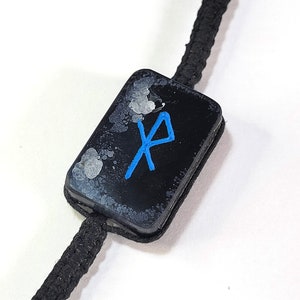 May include: A black and white tag with a blue rune symbol on a black cord.