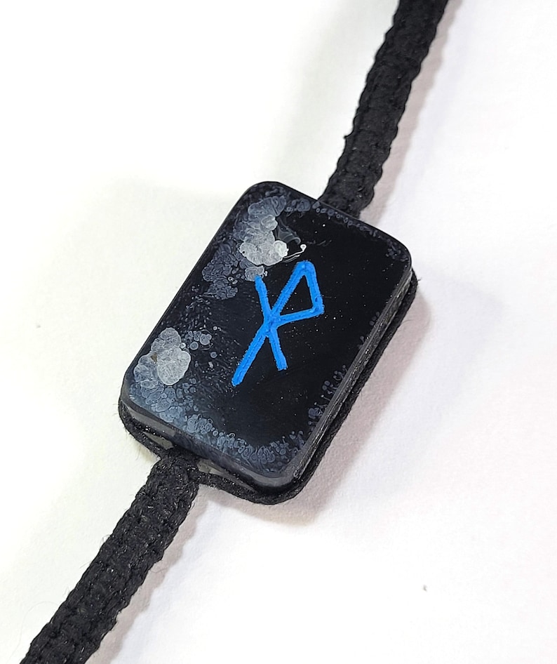 May include: A black and white tag with a blue rune symbol on a black cord.