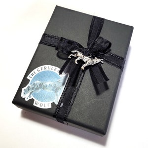 May include: A black gift box with a black ribbon and bow. The box has a sticker with a wolf design and the text "The Cerulean Wolf".