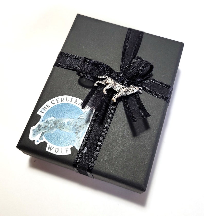 May include: A black gift box with a black ribbon and bow. The box has a sticker with a wolf design and the text "The Cerulean Wolf".