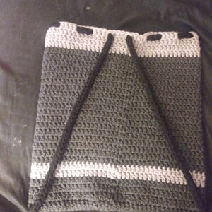 May include: A grey and white crocheted drawstring bag with black drawstrings. The bag is made with a textured stitch and has a simple design.