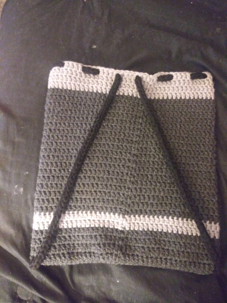 May include: A grey and white crocheted drawstring bag with black drawstrings. The bag is made with a textured stitch and has a simple design.