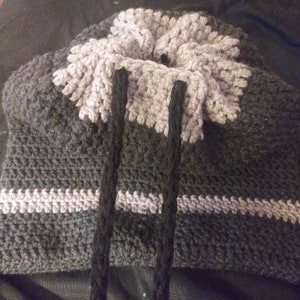 May include: A grey and white crocheted bag with black drawstrings. The bag has a textured pattern and a wide opening at the top.