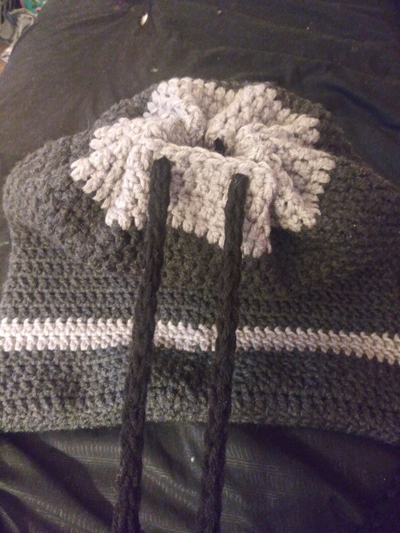 May include: A grey and white crocheted bag with black drawstrings. The bag has a textured pattern and a wide opening at the top.