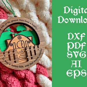 May include: A wooden ornament featuring a depiction of a hobbit hole with a green lawn and a white picket fence. The ornament is round and has the text "In a hole in the ground there lived a hobbit... It was a hobbit-hole, and that means comfort" inscribed around the edge.