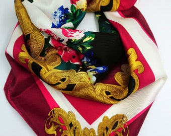 May include: A silk scarf with a floral pattern and gold accents. The scarf is folded in a triangular shape and has a burgundy, white, and black background.