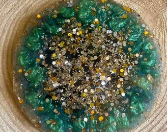 Peut inclure: Un dessous de verre rond en résine verte et dorée avec des paillettes incrustées dans la résine. Le dessous de verre est posé sur une surface en bois.