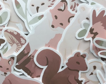 May include: A collection of stickers featuring various woodland creatures, including a fox, squirrel, owl, and mushroom. The stickers are in a pastel pink and brown color scheme.