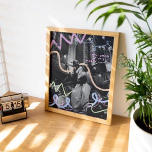 May include: A framed print featuring a black and white photograph of a person singing on stage. The background is a dark, blurred image of a crowd. The print has colourful lines and the text "It's okay if it's messy" written on it.