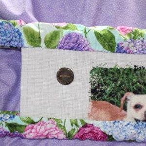 May include: A cross-stitch project in a wooden embroidery hoop with a floral fabric border. The project depicts a brown and white dog with floppy ears lying in a grassy area.
