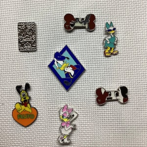 May include: A collection of seven Disney character enamel pins. The pins feature Pluto, Donald Duck, Daisy Duck, and a bone with a dog on it. The pins are all different colors and have a variety of designs.