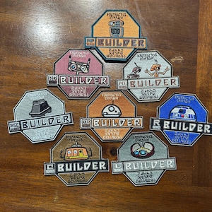 May include: Nine embroidered patches featuring various Star Wars characters and the text "BUILDER SERIES". The patches are in different colors, including orange, blue, red, and gray. Each patch features a different character, including R2-D2, a droid, and a robot.