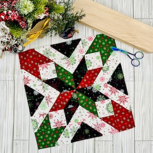 Może przedstawiać: Biały blok kołdry z tkaniny z wzorem gwiazdy w kolorze czerwonym, zielonym i czarnym. Blok kołdry składa się z mniejszych kwadratów i trójkątów.