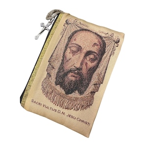 May include: A beige rectangular zippered pouch featuring a woven image of the face of Jesus on a cloth. The pouch has a gold-colored trim and a silver-toned crucifix charm attached to the zipper pull. The text SACRI VULTUS D.N. JESU CHRISTI is printed.