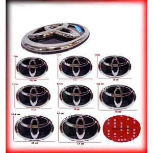 May include: A collection of eight oval Toyota vehicle emblems with a chrome finish and black background, displayed with various width measurements ranging from 10.0 cm to 17 cm, alongside one emblem showing the red adhesive backing.