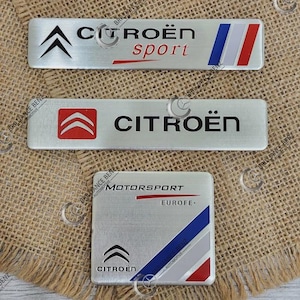 May include: Three rectangular metal automotive emblems featuring the Citroën logo. The top emblem reads Citroën sport with a blue, white, and red stripe. The middle emblem displays the Citroën logo and text. The bottom square emblem reads Motorsport Europe.