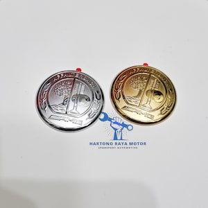 May include: Two circular automotive emblems featuring the Affalterbach crest, one in a polished silver finish and one in a gold finish. Each emblem displays a tree and a valve design with the text AMG and Affalterbach embossed on the surface.