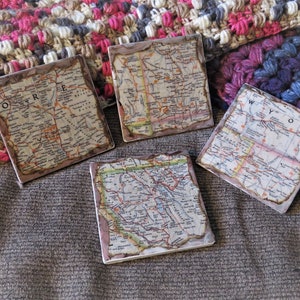 May include: Four square ceramic coasters with vintage maps of Oregon, Wyoming, Idaho, and Montana. Each coaster features a detailed map with roads and cities.