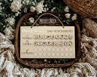 May include: A wooden daily responsibilities chart with the name "Ozzy's" in white letters. The chart includes morning and evening routines with illustrated icons and space for tracking completion. A rope is attached for hanging.