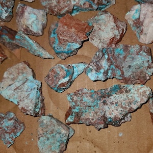 May include: A collection of rough, natural turquoise stones with a brown matrix. The stones have a blue-green color and are irregularly shaped.