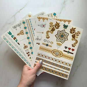 May include: A set of eight gold and turquoise temporary tattoo sheets with various designs, including geometric patterns, floral motifs, and a mandala. The sheets are labeled "YH-002".