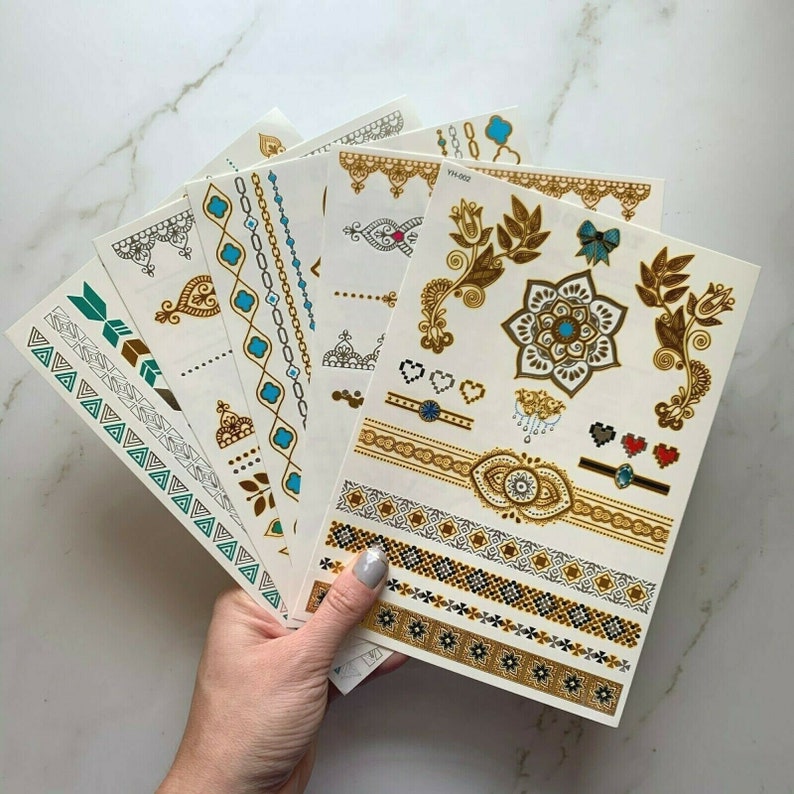 May include: A set of eight gold and turquoise temporary tattoo sheets with various designs, including geometric patterns, floral motifs, and a mandala. The sheets are labeled "YH-002".