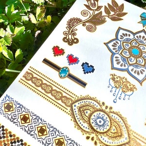 May include: A sheet of temporary tattoos with a variety of designs, including hearts, flowers, and geometric patterns. The tattoos are gold, silver, blue, red, and turquoise.