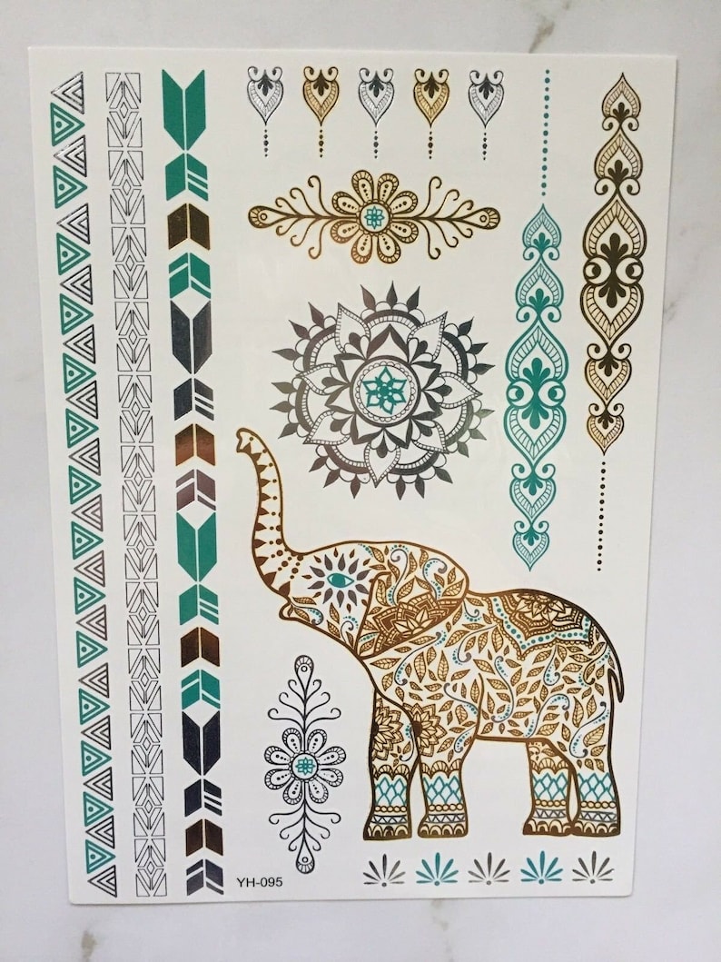 May include: A sheet of temporary tattoos featuring an intricate gold elephant design with teal and silver accents. The sheet also includes several smaller designs, including a mandala, flowers, and geometric patterns. The text "YIH-095" is printed in the bottom left corner.