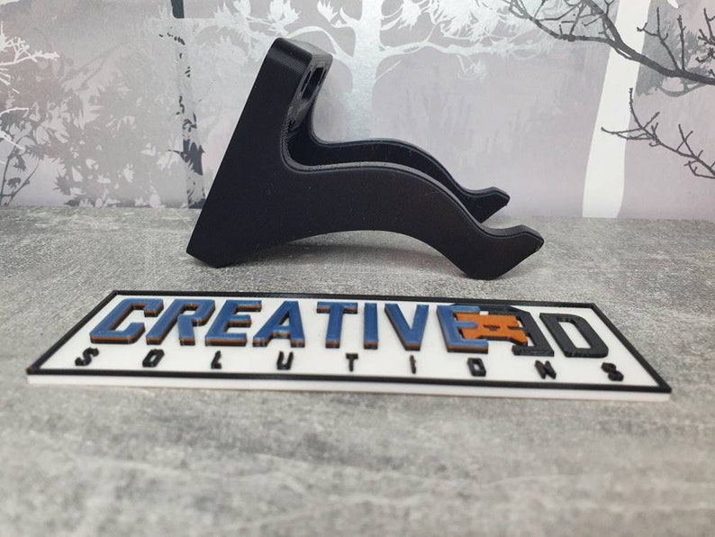 May include: Black plastic wall mount for a guitar or other instrument. The mount is curved to fit the shape of the instrument. The mount is designed to be attached to a wall.