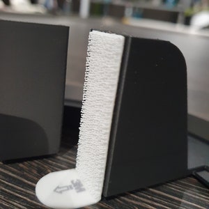 May include: A black plastic corner protector with a white adhesive strip. The adhesive strip has a white arrow pointing upwards and the text "3M" printed on it.