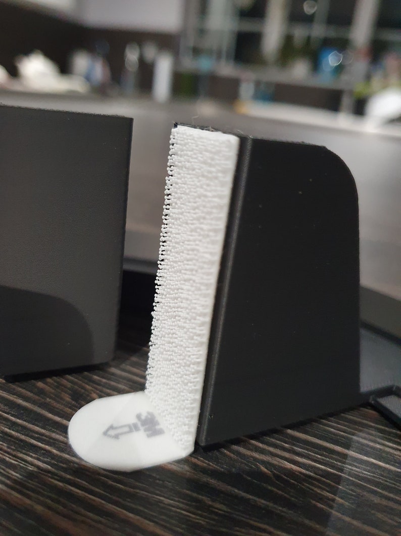 May include: A black plastic corner protector with a white adhesive strip. The adhesive strip has a white arrow pointing upwards and the text "3M" printed on it.